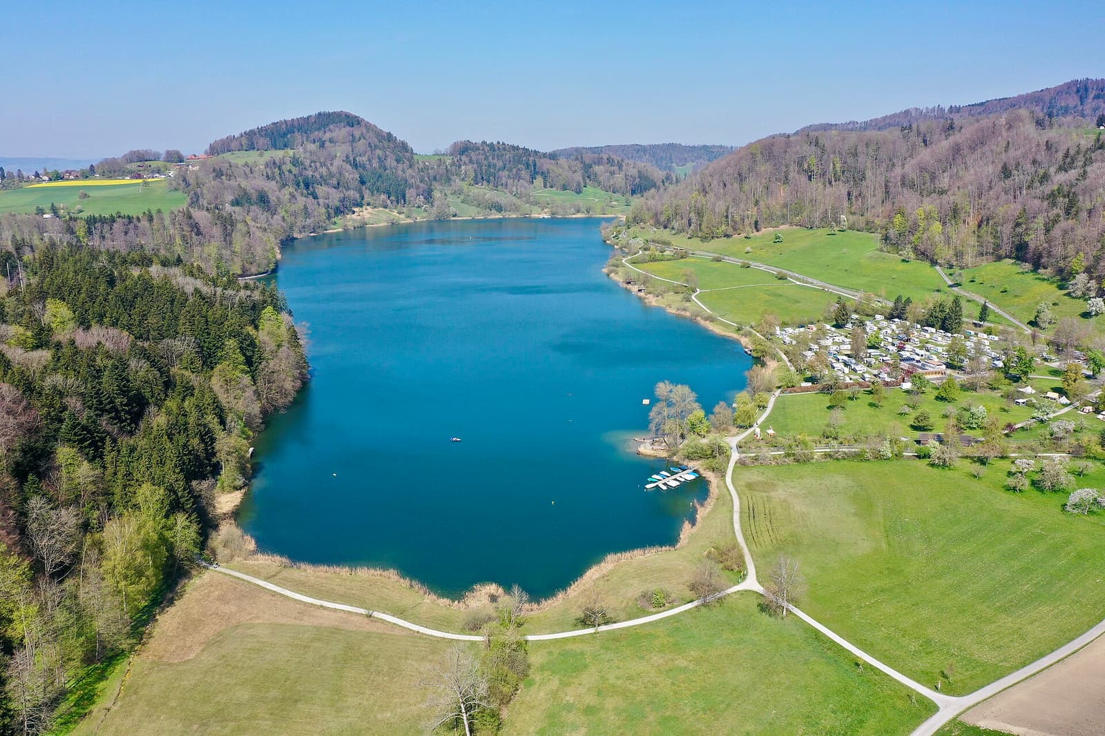 Vue aérienne du lac turquoise du Türlersee, entre champs verts et collines boisées