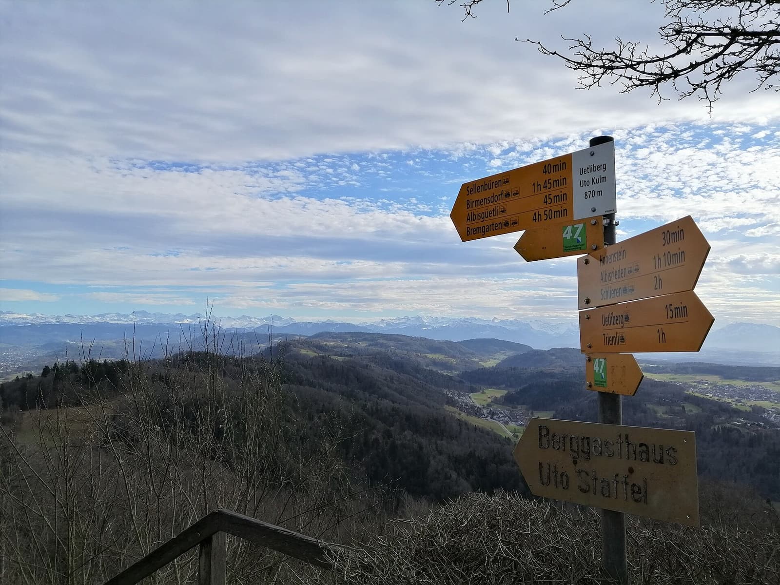 Panneaux jaunes de randonnée près du sommet, avec une large vue sur des collines boisées