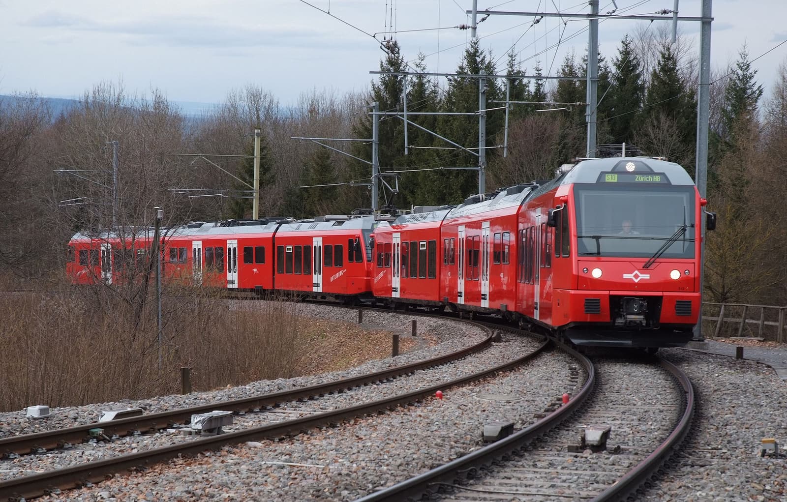 Un train rouge de la SZU dans la courbe d’entrée de la gare d’Uetliberg, entre des arbres dénudés